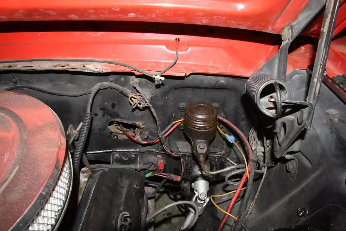 An older model jam-jam single reservoir brake master cylinder located under the hood of a red vehicle.