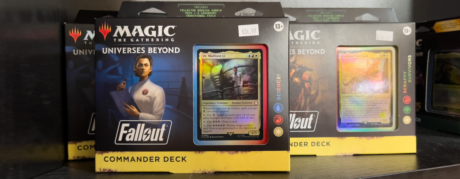 Auf einem Regal stehen mehrere Magic: The Gathering - Universes Beyond: Fallout Commander-Decks in ihrer Originalverpackung mit sichtbaren Kartenfenstern.