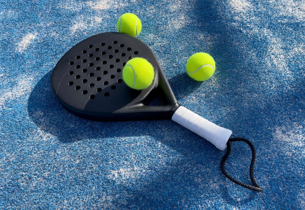 Black padel racket with three green balls on blue court