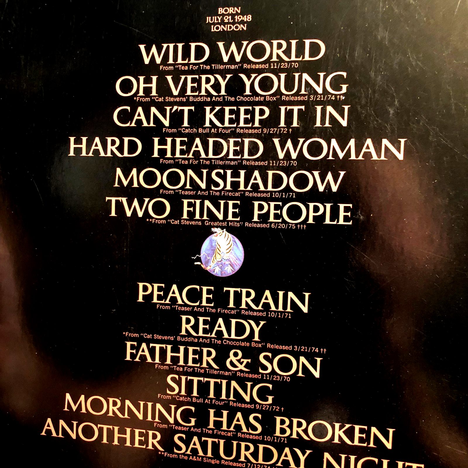 Cat Stevens Greatest Hits Lp poster with song titles, “Born in 1948 London” text, and blue-toned abstract background.