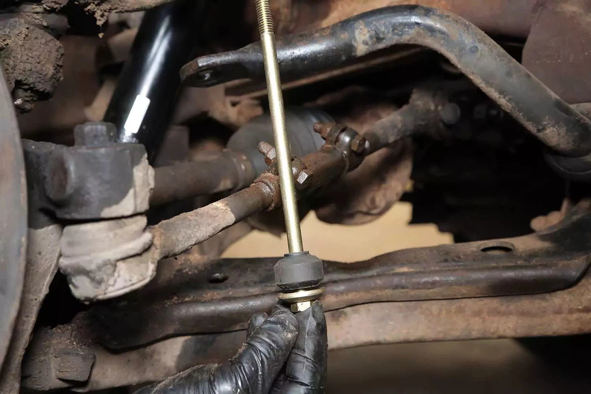 A mechanic holds the end link assembly with only the lower washer and bushing in place.