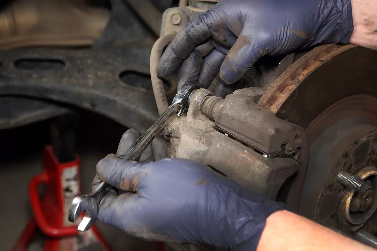 A mechanic uses a wrench on a brake caliper bolt.