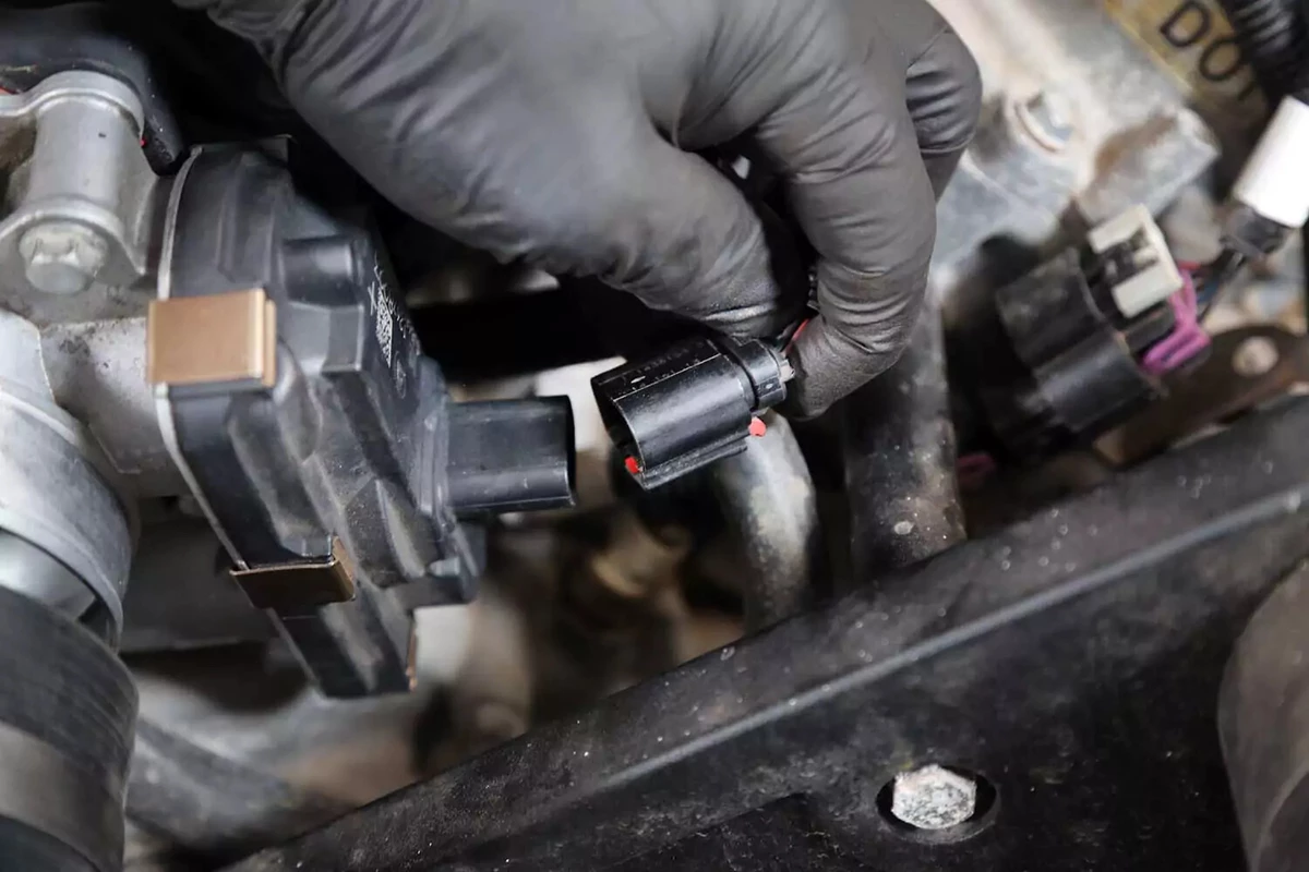 A mechanic removes the plug connecting the throttle body with the ECM.
