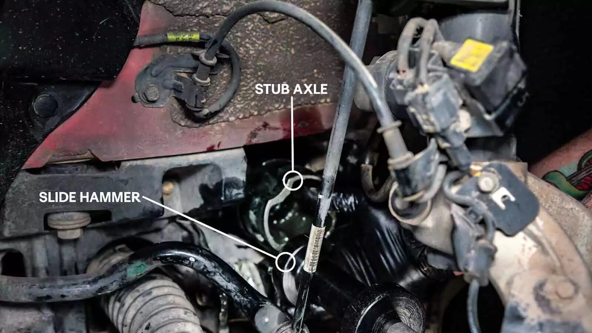 An annotated photograph shows a mechanic engaging a slide hammer to release the stub axle. Annotations call out the slide hammer and stub axle.