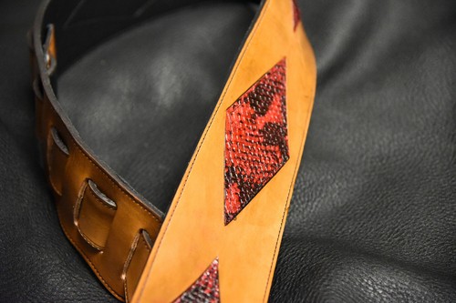 Brown leather guitar strap with red diamond inlay made of tan fabric, featuring two fastening holes and black strap.
