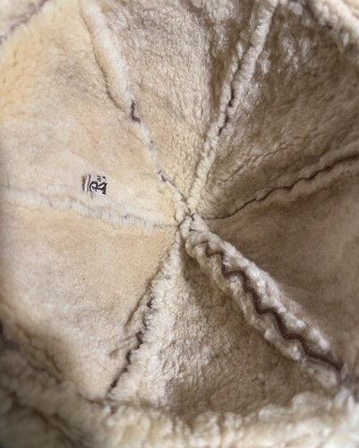 Brown shearling-lined vintage ranchero bucket hat with creased front seam and small white “R” patch on the side.