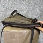 Brown canvas crossbody bag with front zipper pocket, black straps, and visible stitching on a cardboard box.