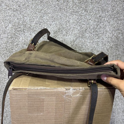 Brown canvas crossbody bag with front zipper pocket, black straps, and visible stitching on a cardboard box.