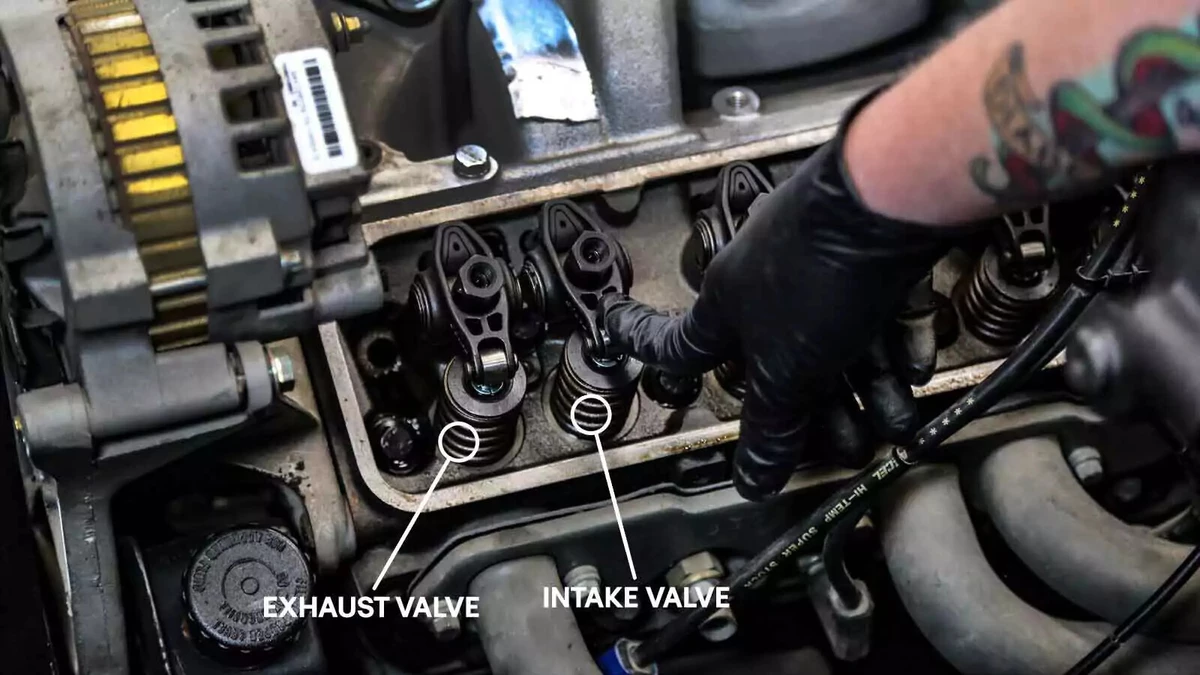 A mechanic points to the first cylinder’s intake valve. Annotations call out the location of the first cylinder’s exhaust and intake valves.