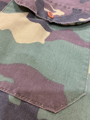 1980s vintage camouflage ranger shirt with green and brown patterns, red button, and dark green stitching on front pocket.