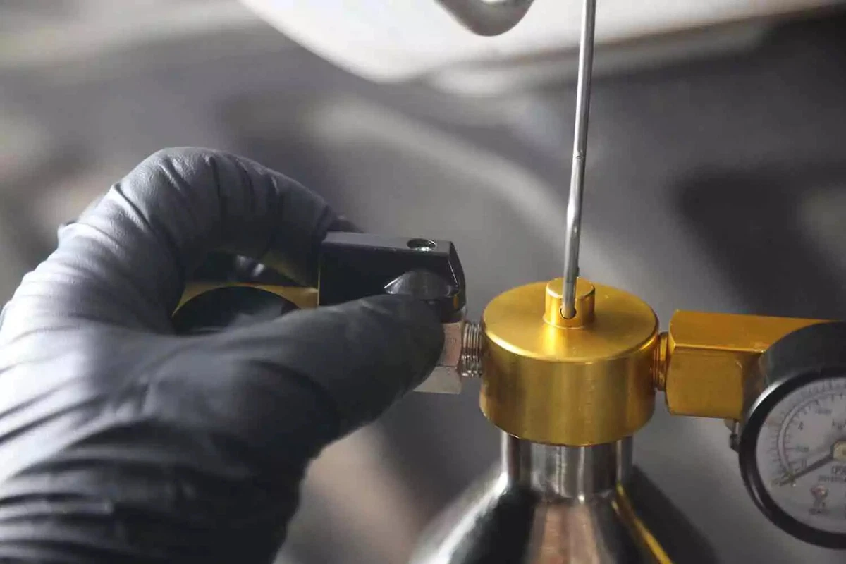 A mechanic wearing black gloves closes the valve of the feed line.