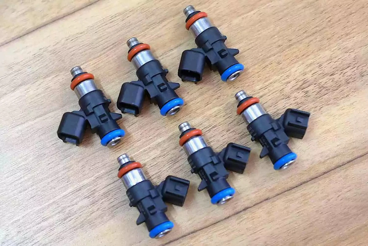 A set of six OEM Pentastar V-6 fuel injectors, displayed on a wood surface.