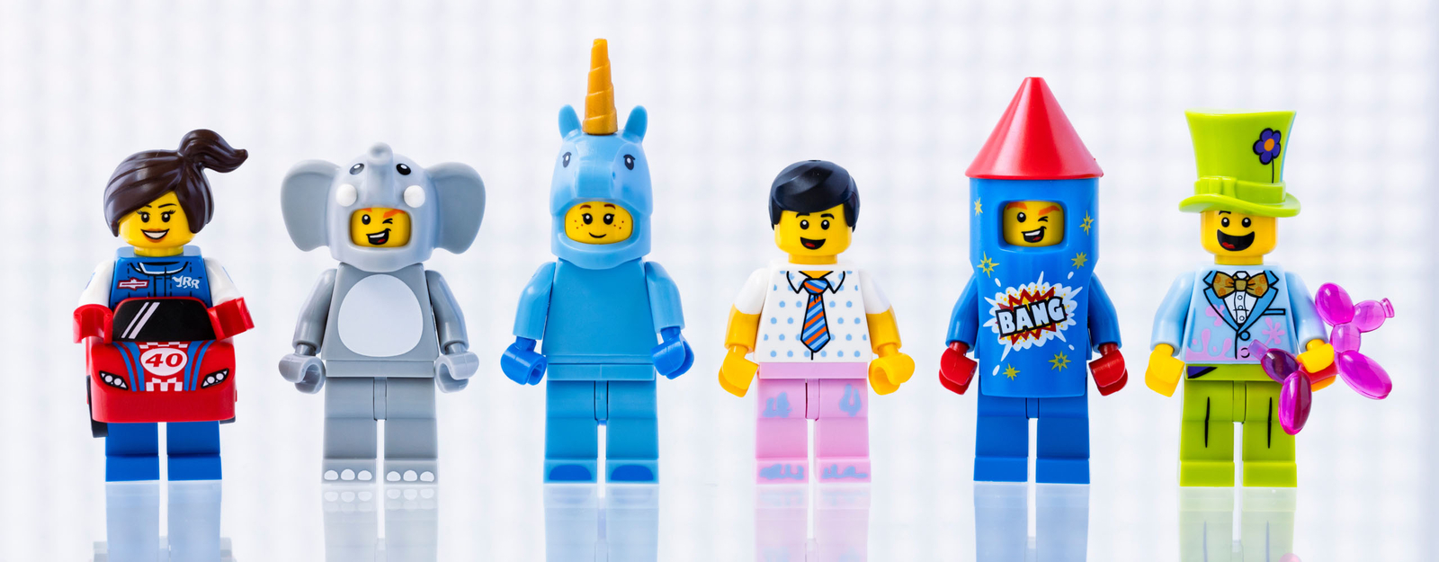 Sechs bunte LEGO Minifiguren in verschiedenen Kostümen, darunter Rennfahrer, Elefant, Einhorn, Geschäftsmann, Rakete und Zirkuskünstler