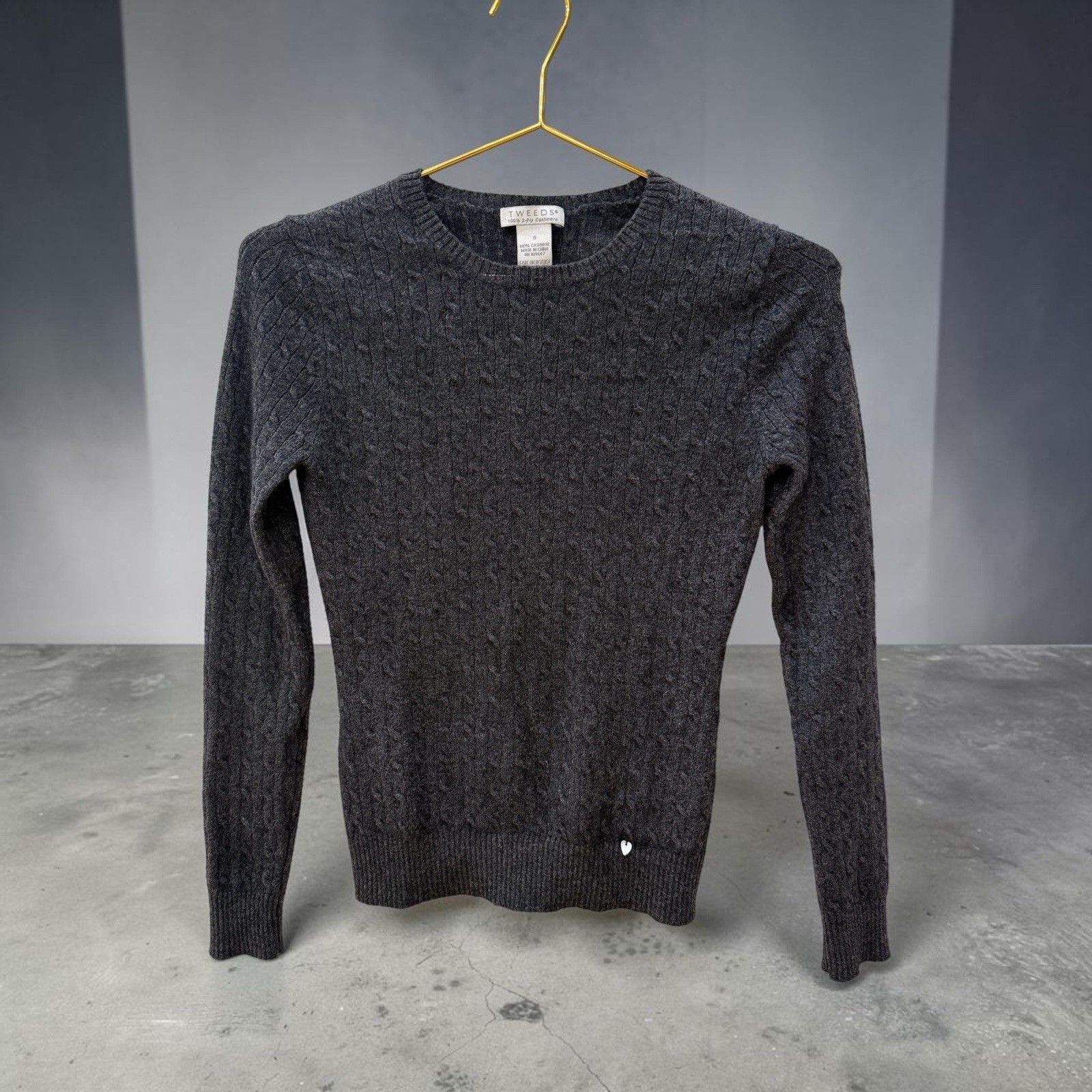 Heathered charcoal cable-knit cashmere sweater on a hanger.
