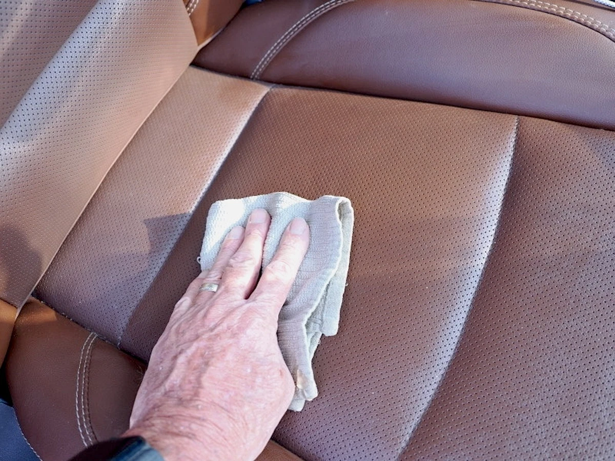 Applying leather conditioner to tan perforated upholstery with a white towel.