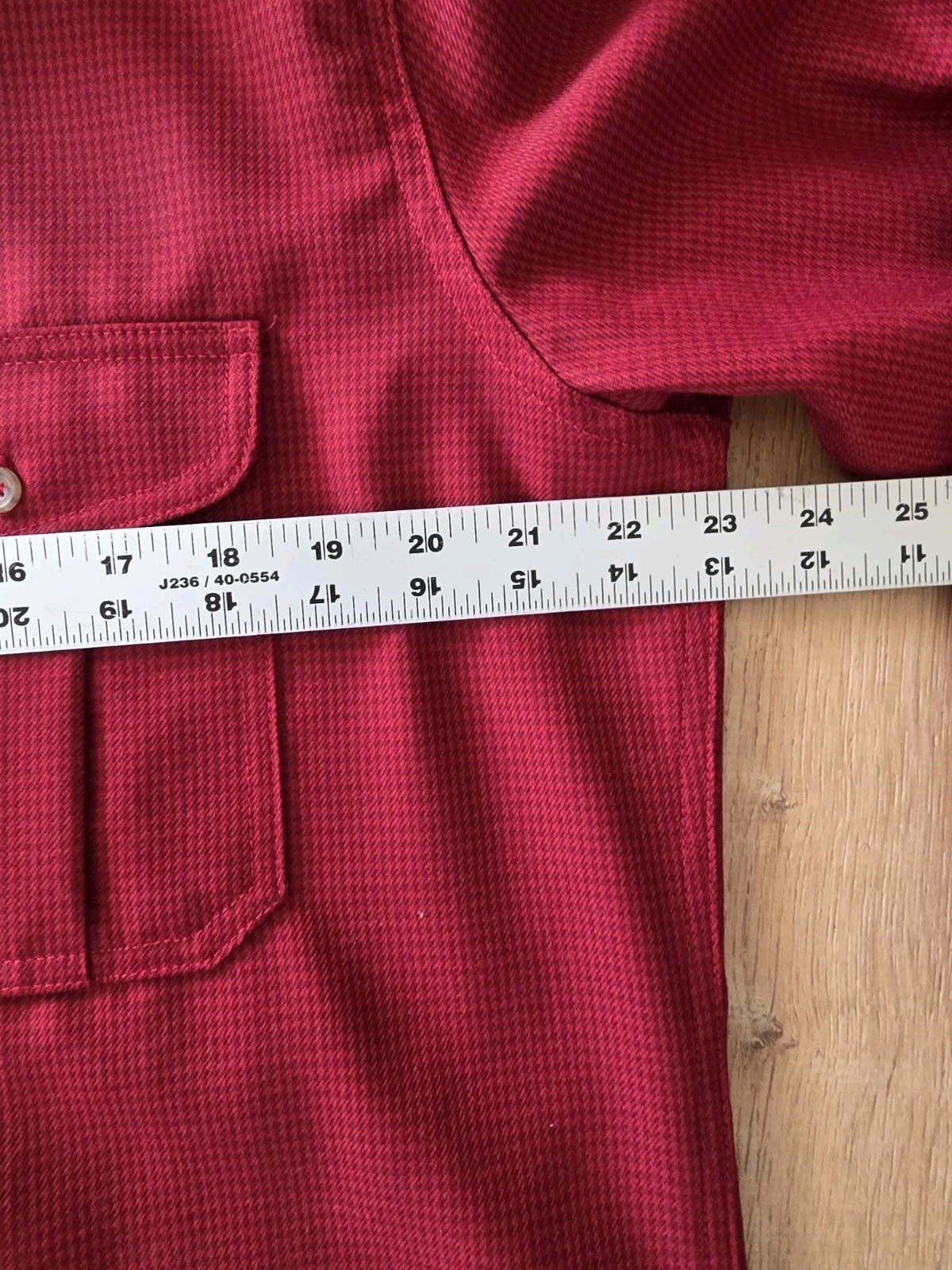 Red Filson virgin wool shirt with two front chest pockets, button-down collar, and white measuring tape across the chest.