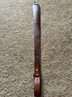 Brown leather leather rifle sling with smooth finish and brass screw holes, resting on a beige carpet.
