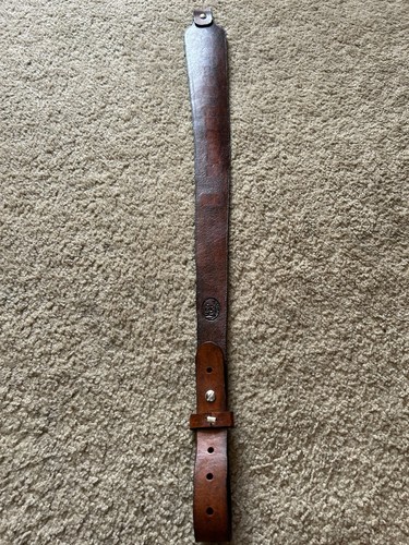 Brown leather leather rifle sling with smooth finish and brass screw holes, resting on a beige carpet.