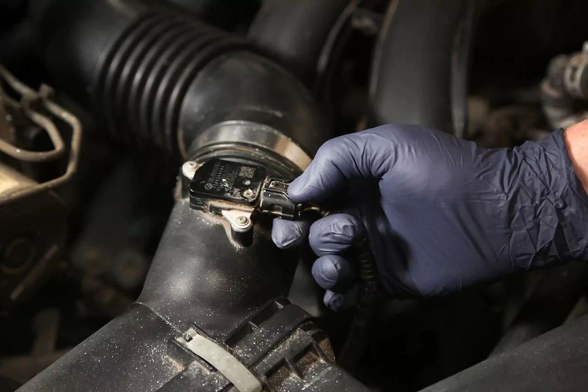 A mechanic removing a wiring harness from an MAF sensor.