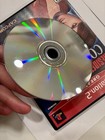 Hand holding a Resident Evil Code Veronica PS2 game disc with rainbow-colored dots and black label reading “Greatest Hits.”
