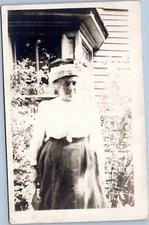 RPPC Scowling woman in front of house