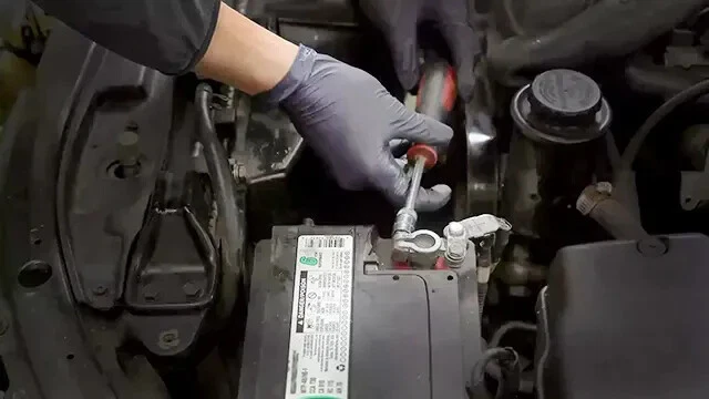 Mechanic wearing latex glove disconnecting negative battery terminal.