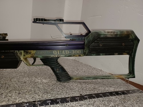 Barnett QUAD-300 System 4 crossbow with purple and green camouflage pattern, mounted scope, and visible branding text.