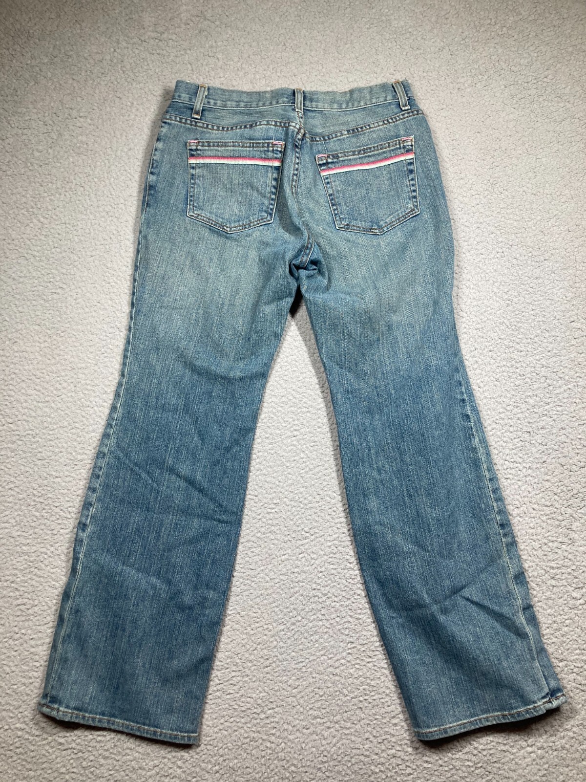 Blue stretch light wash Karen Kane women’s jeans with pink and red stripe details on back pockets, laid flat on gray surface.