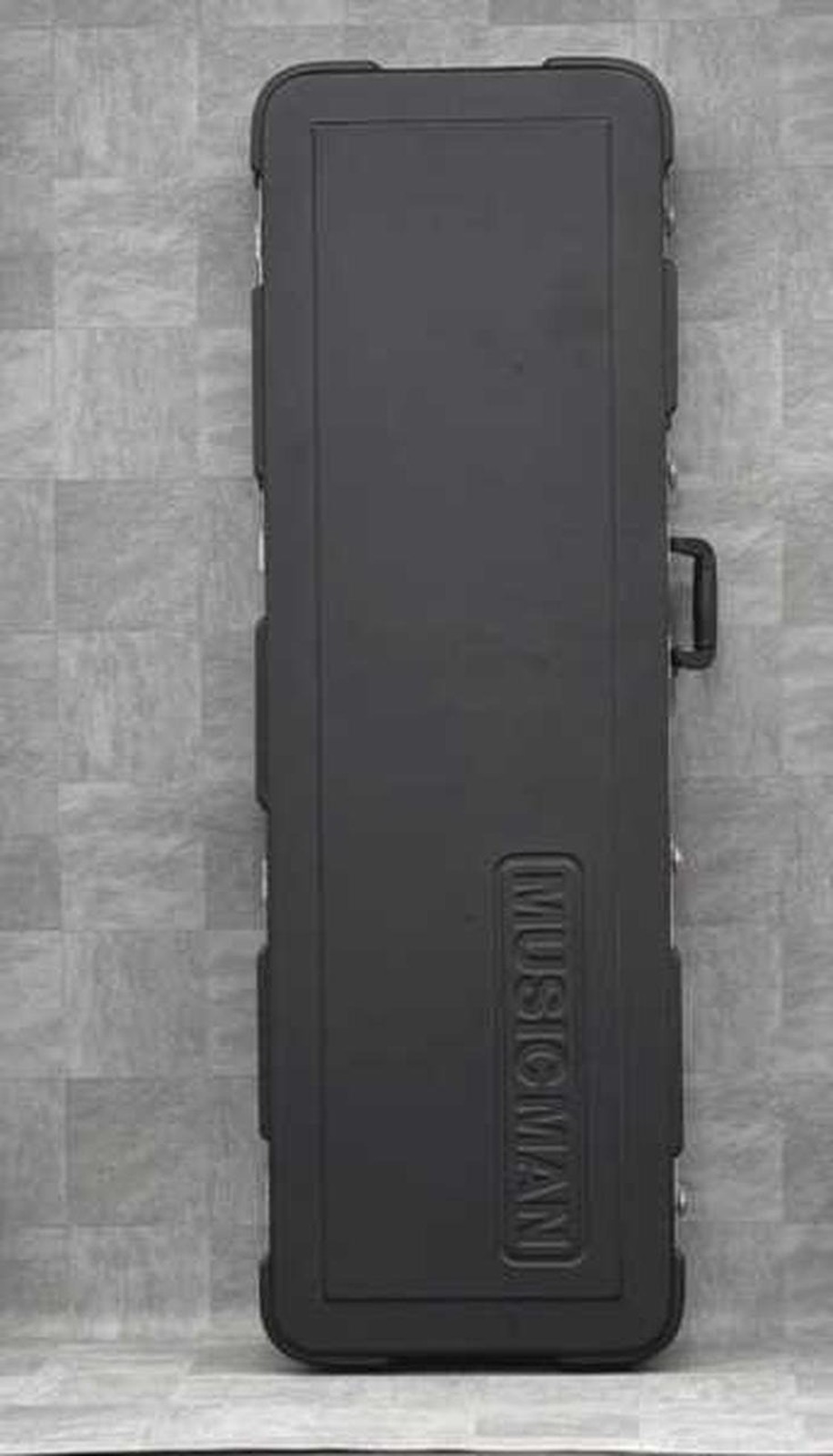 Black Ernie Ball Musicman STINGRAY used ash body guitar with maple neck, hard shell case on gray textured surface.