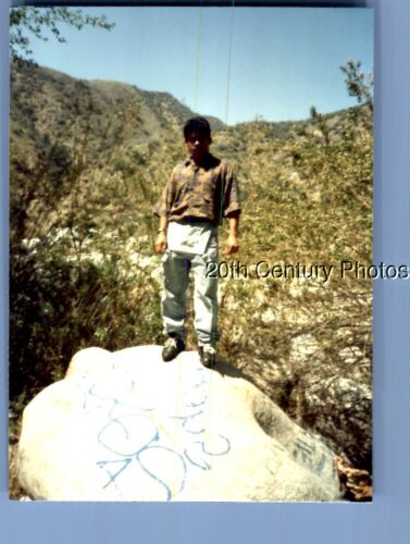 FOUND COLOR PHOTO O+1860 MAN POSED ON ROCK WITH GRAFFITI - Picture 1 of 1