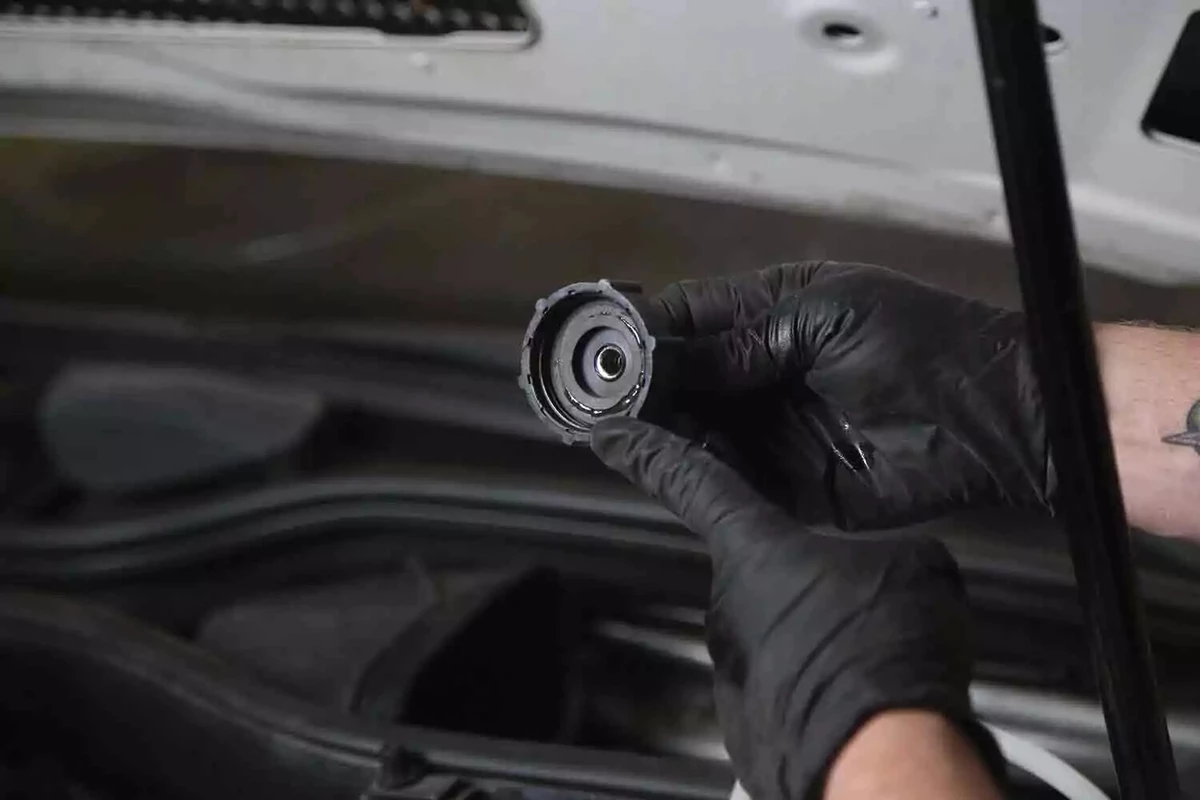 A mechanic wearing black gloves holds the screw cap from a brake bleeder kit.