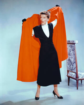 Katharine Hepburn wearing a black dress as she puts on a red coat - Old Photo