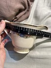 Cream ceramic mug with gold rim, floral print, and two measurement markings in centimeters on a light fabric surface.