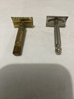 Two vintage Gillette safety razors, one brass with flat rectangular head and one silver with flat rectangular head and black handle.