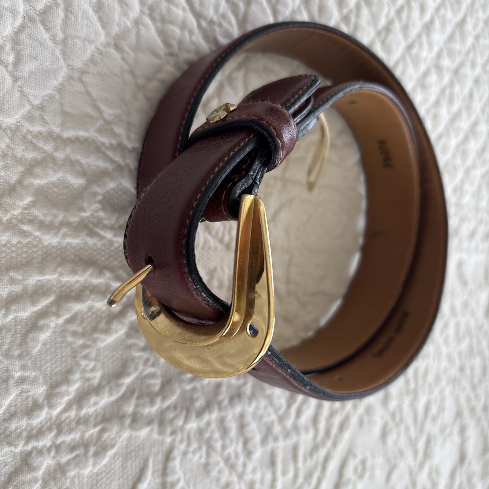 Oxblood leather belt coiled with a brass buckle.