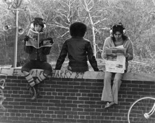 Three girls, each wearing headphones as they sit on a wall, with on - Old Photo