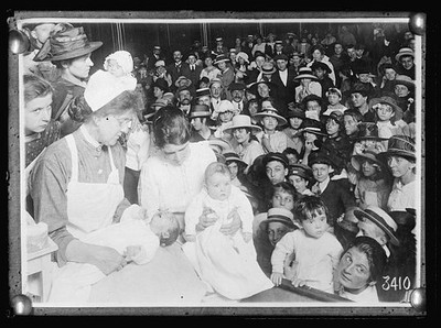 Nurse showing an audience of working people how to bathe and dress a baby