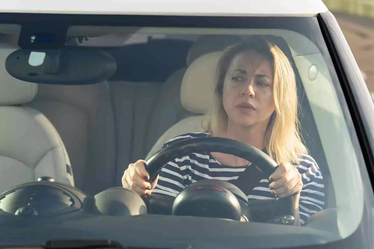 A female driver wearing a black and white striped shirt looks concerned.