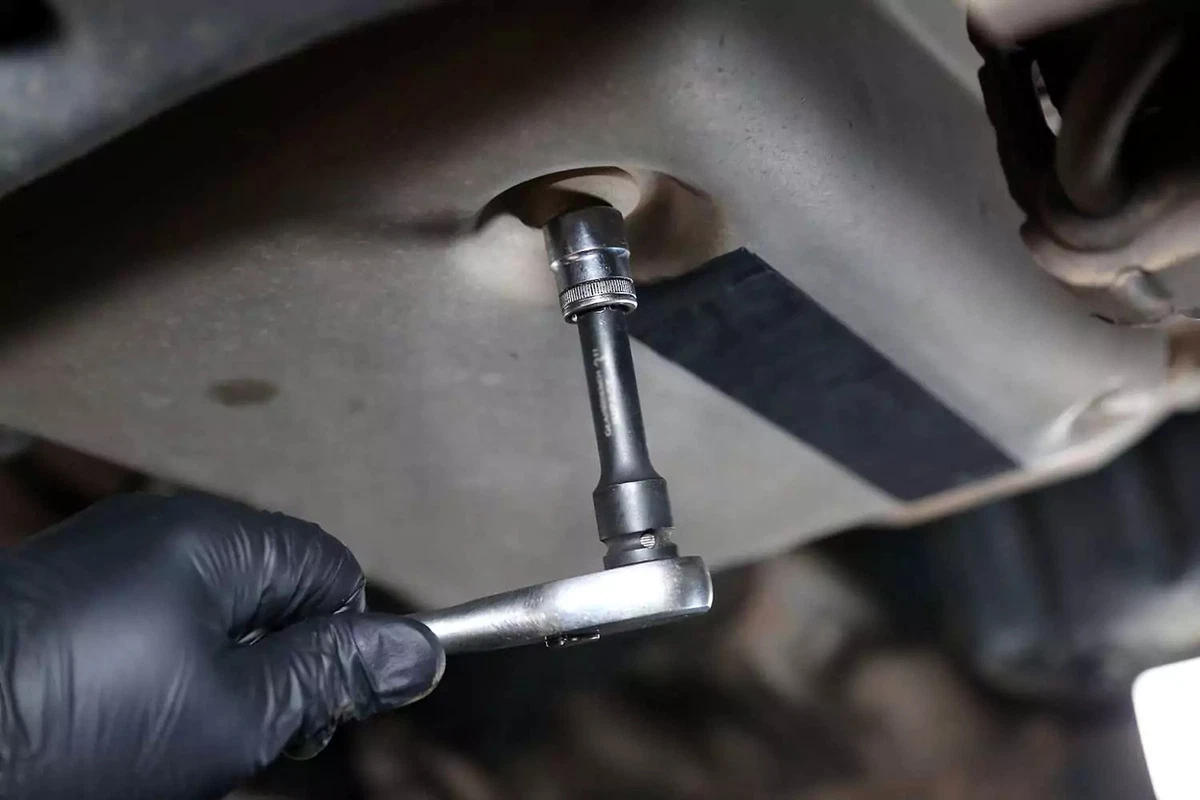 A mechanic loosens the automatic transmission drain plug with a socket wrench.