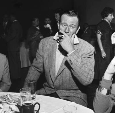 John Wayne smokes a cigarette at a party 1955 OLD MOVIE PHOTO