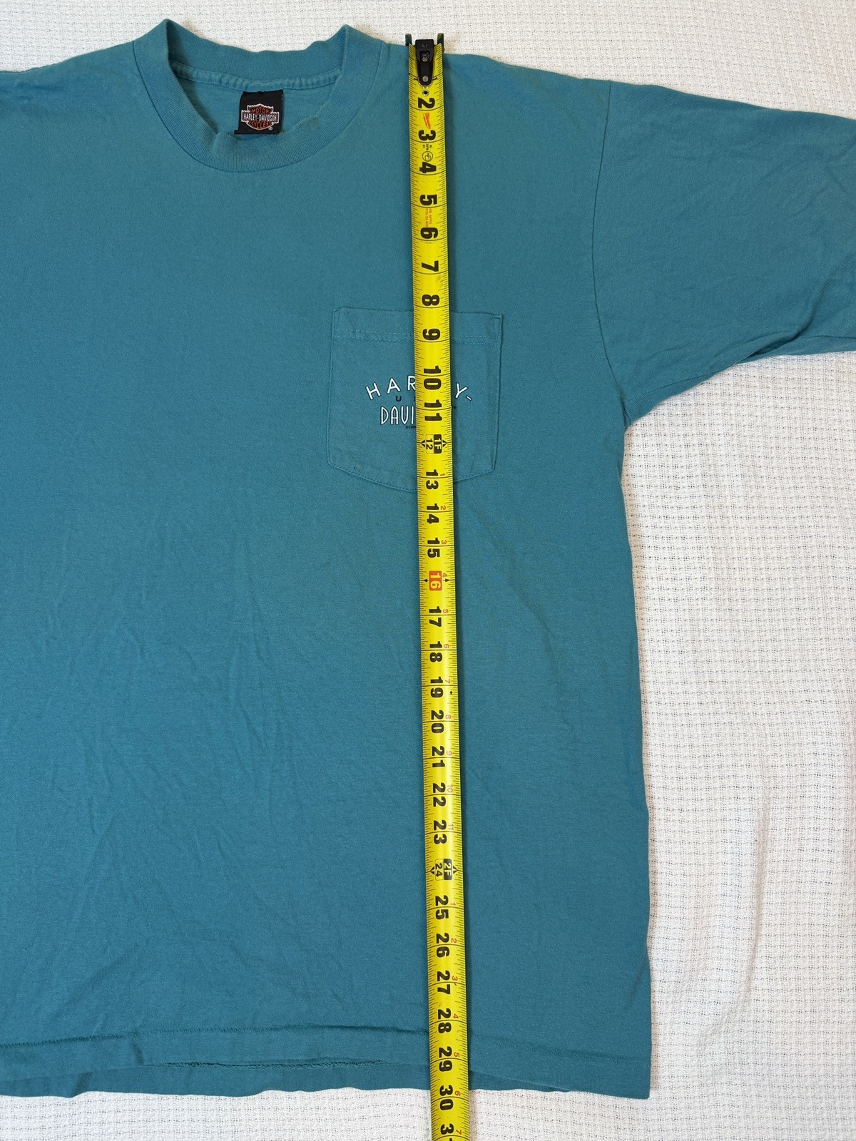 Teal Harley-Davidson men’s XL T-shirt with front pocket, yellow measuring tape, and white “Made in U.S.A.” text.