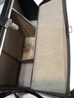 Black leather shoulder bag with visible seams, open to show a tan fabric lining with dark stains on a wooden surface.