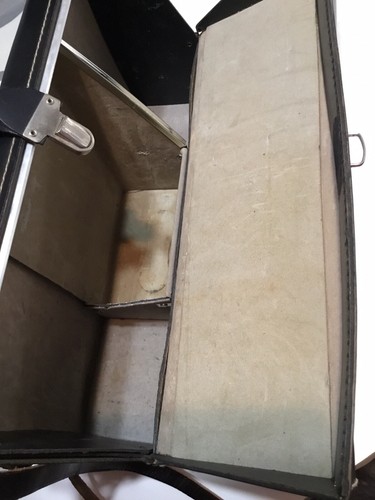 Black leather shoulder bag with visible seams, open to show a tan fabric lining with dark stains on a wooden surface.