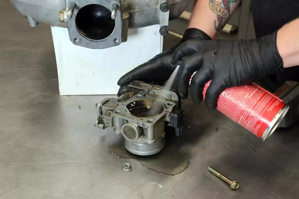 A mechanic sprays aerosol cleaner into the throttle body to remove varnish and carbon.