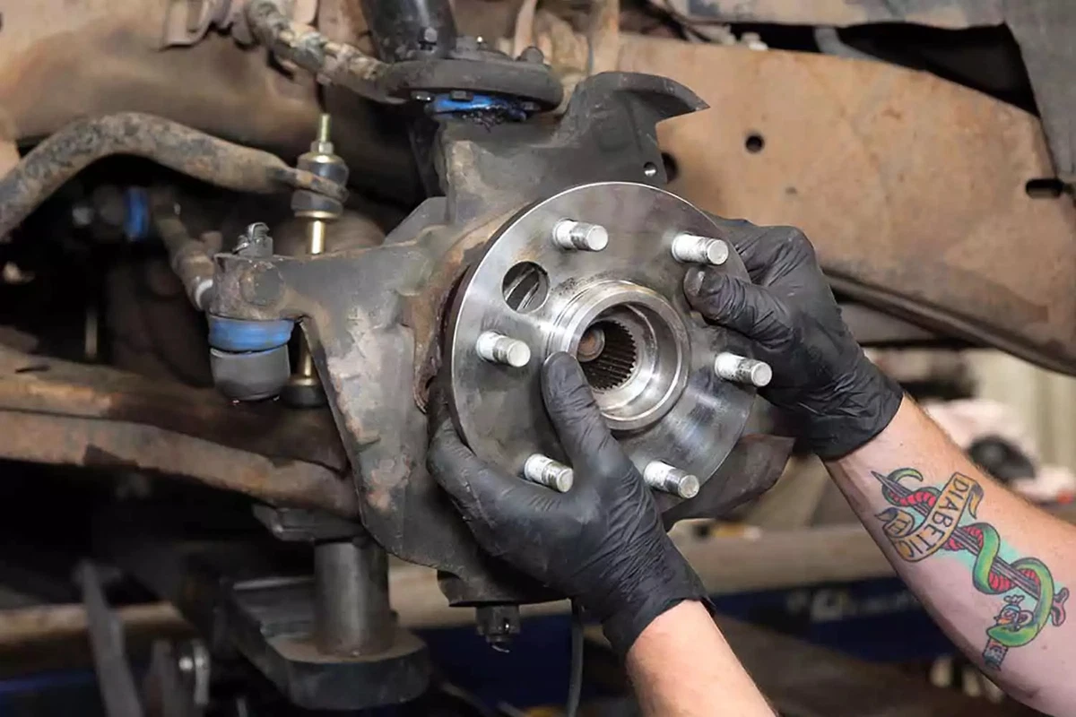 A mechanic slides the new wheel bearing hub into the knuckle.