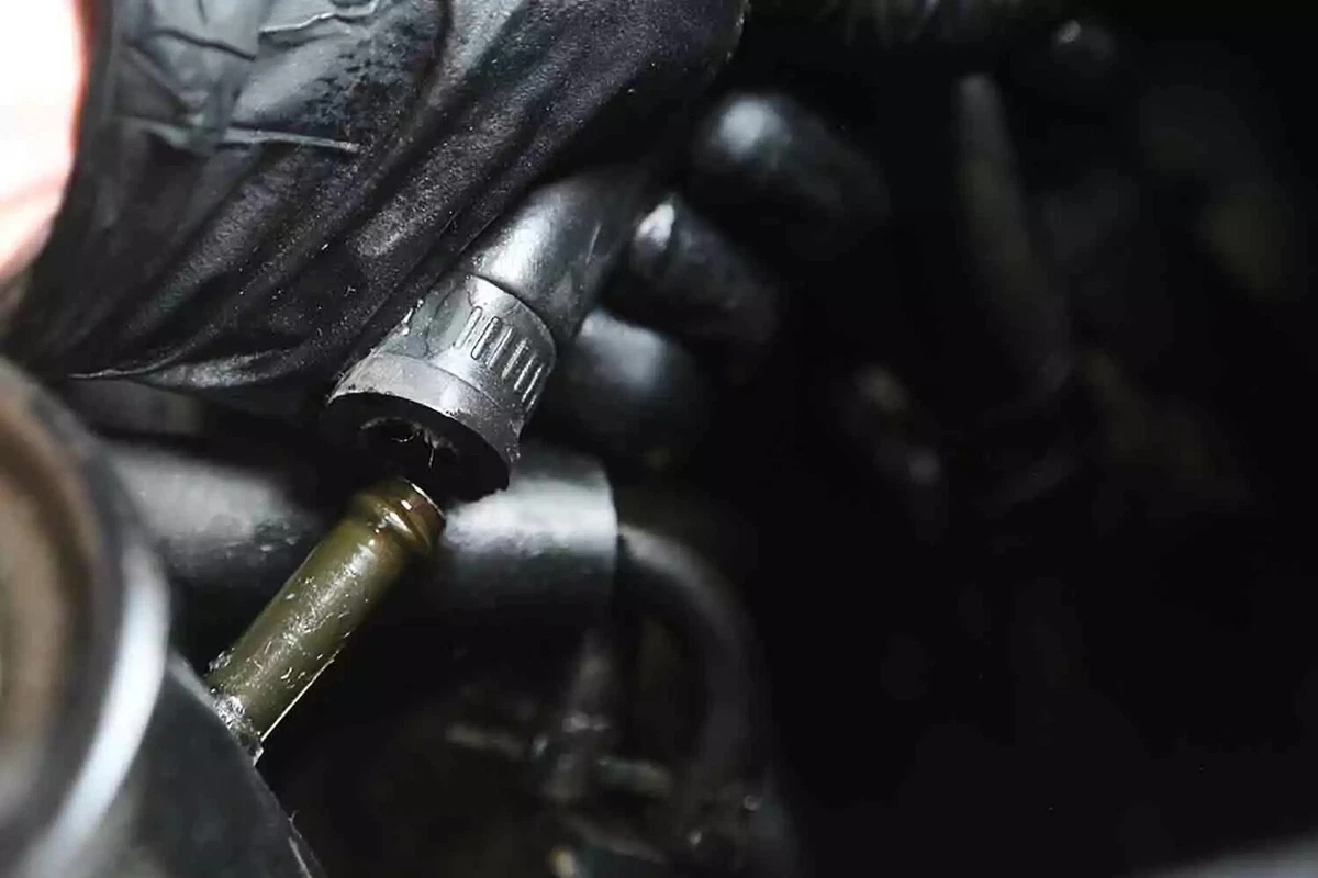 A mechanic wearing a black glove reinstalls the return line to the vehicle's power steering fluid reservoir.