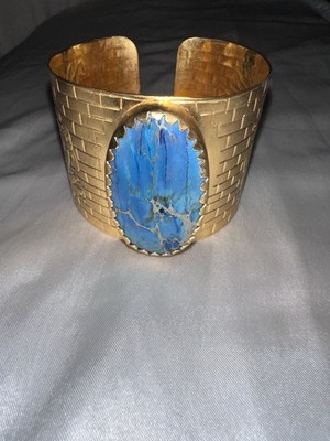 Gold-tone cuff bracelet with a bold blue stone and elegant engraved details.