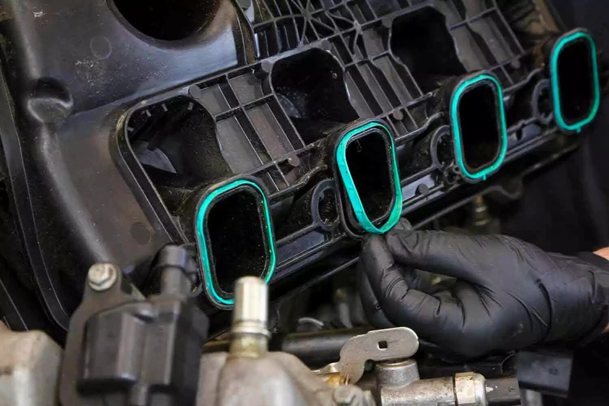A close-up view of a mechanic wearing a nitrile glove installing teal-colored O-ring intake manifold gaskets on a modern engine.