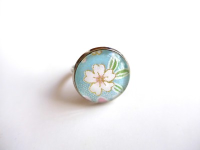 Runder Ring mit weißem Blumenmuster auf himmelblauem Hintergrund, japanisch inspiriert.
