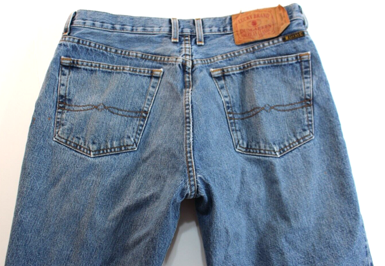 Back view of VTG Lucky Brand jeans in medium wash brown with paint splatter on right leg and tan leather patch on waistband.